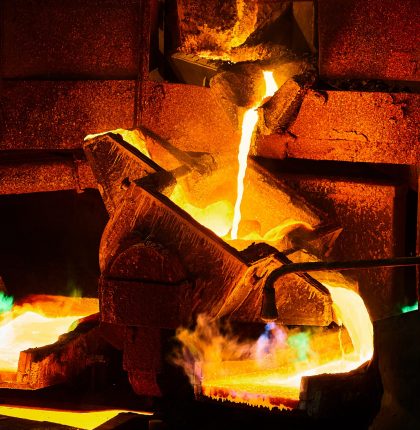 Pouring liquid molten copper metal for anodes into form on casting wheel in dark metal-processing workshop extreme close view